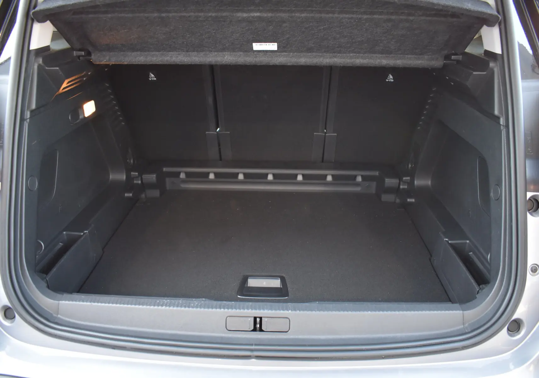 Coffre ouvert vu de l'arrière d'un Citroën C5 Aircross 2024 gris métallisé, espace de chargement spacieux et propre.