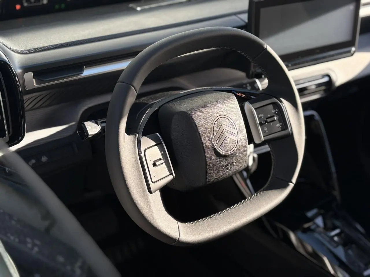 Vue rapprochée du volant multifonctions noir du Citroën C3 Aircross Hybrid 2025 avec tableau de bord gris sidérite.