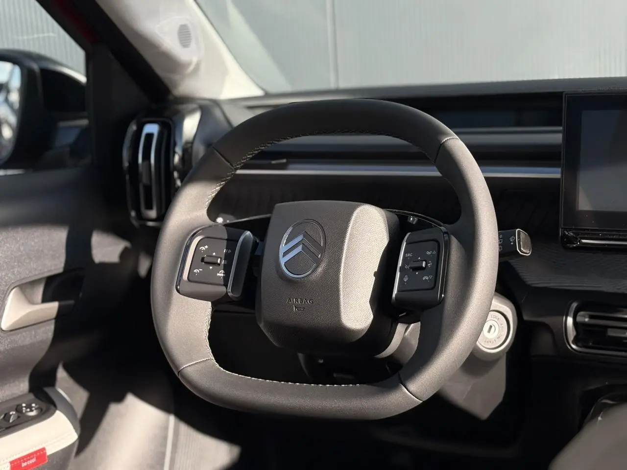 Volant multifonctions Citroën vu de face dans l'habitacle sombre, avec tableau de bord et écran tactile partiellement visibles.