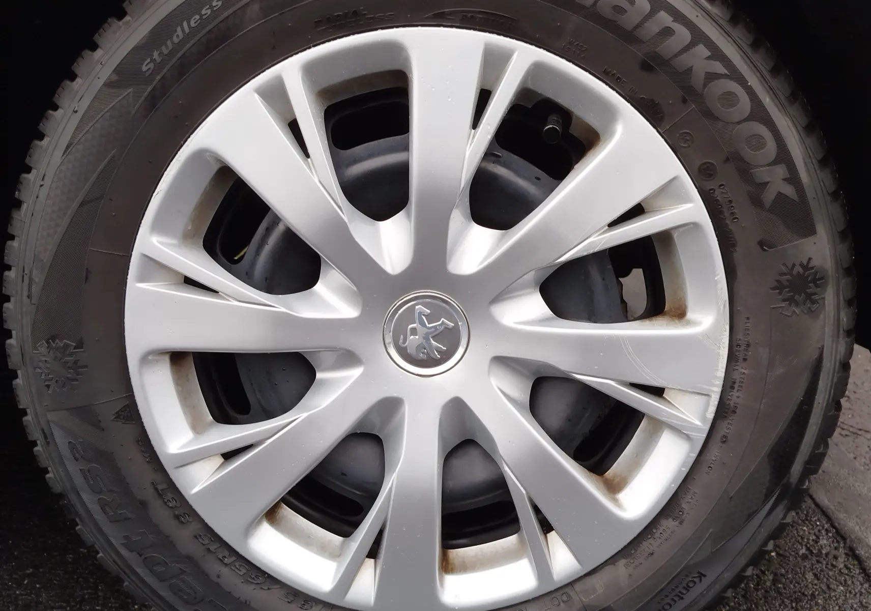 Gros plan sur la jante argentée d’une roue de Peugeot 208 noire, avec logo lion au centre et pneu hiver Hankook.