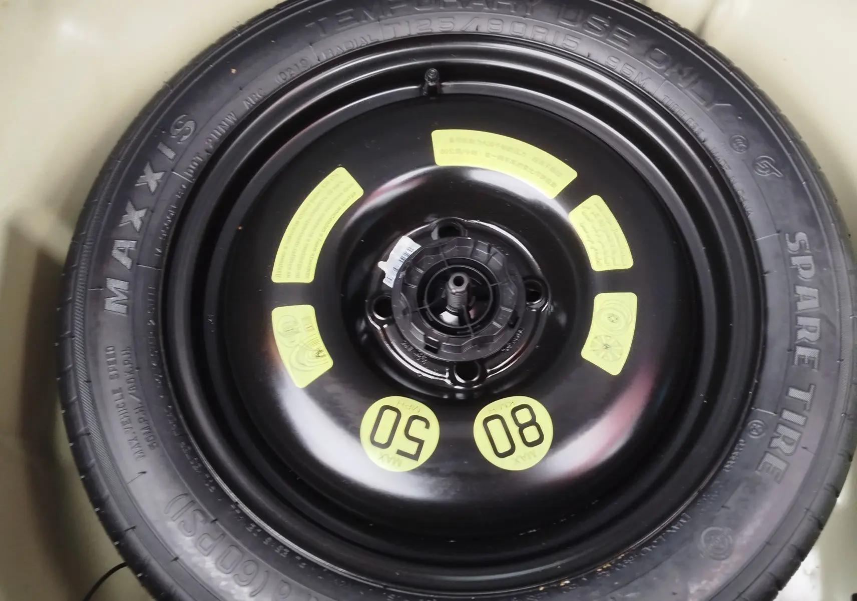 Gros plan sur la roue de secours noire Maxxis montée dans le coffre d'une Peugeot 208 noire de 2019.