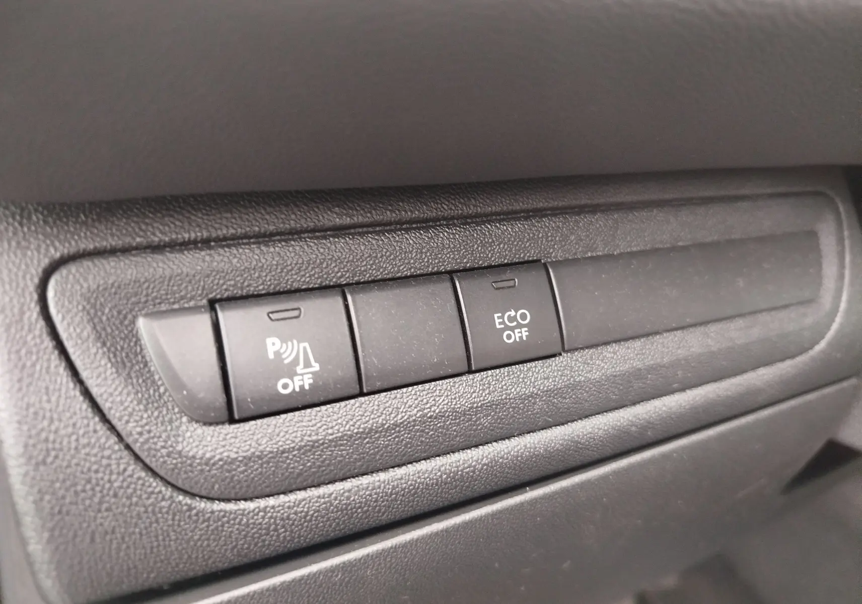 Gros plan sur les boutons de commande du tableau de bord noir de la Peugeot 208 Diesel, avec fonction ECO et parking désactivée.