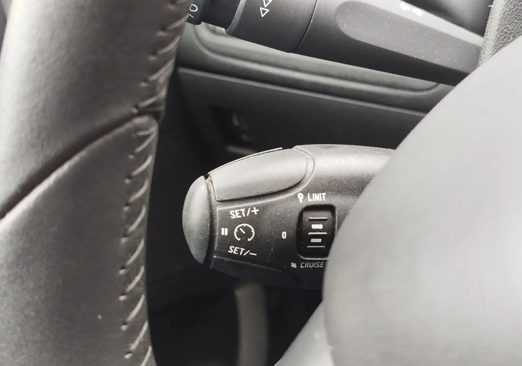 Gros plan sur le commodo de régulateur de vitesse à gauche du volant d’une Peugeot 208 noire, intérieur sombre.
