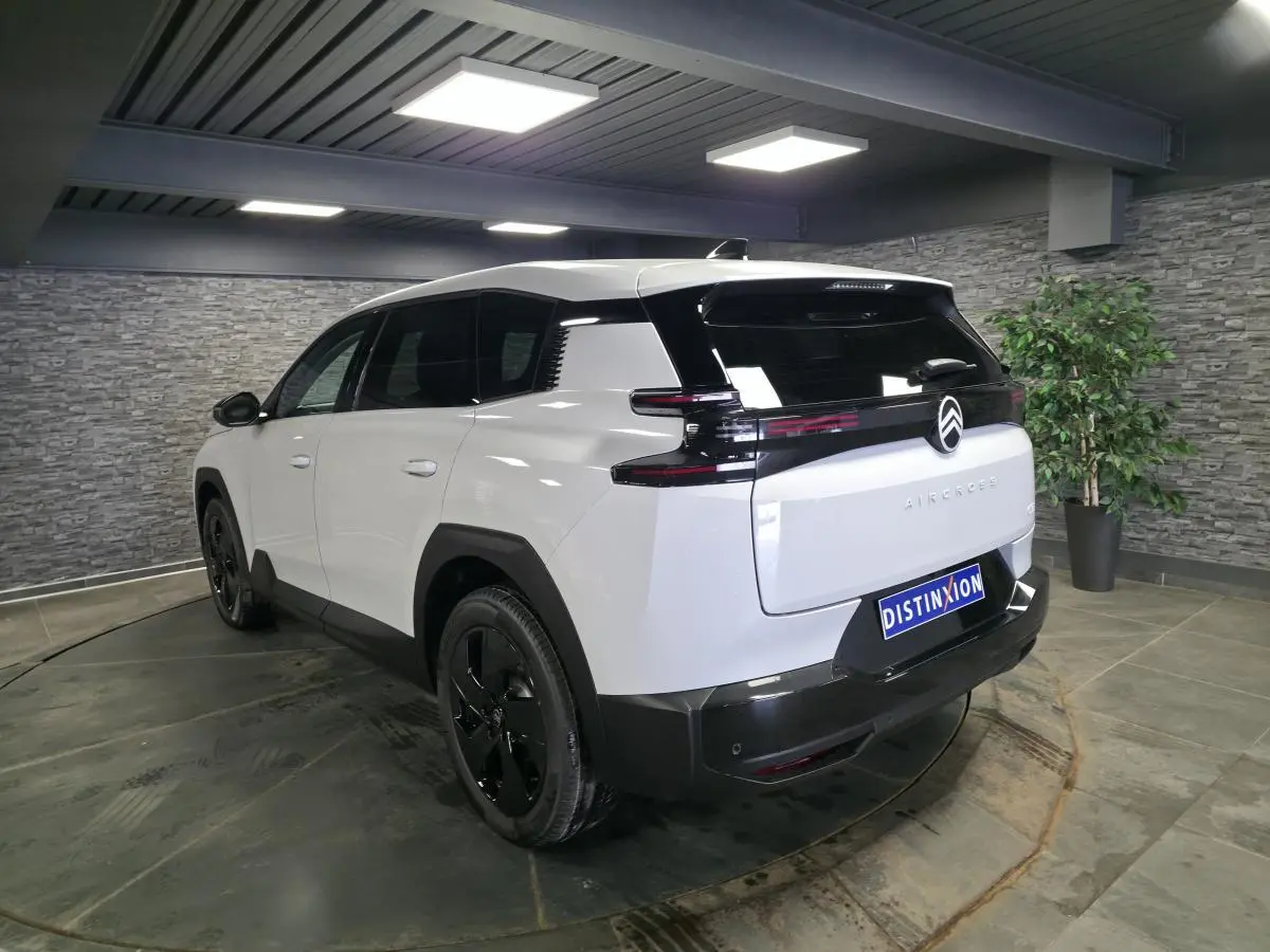 Vue 3/4 arrière droite du Citroën C5 Aircross blanc avec toit noir et jantes alliage noires en intérieur showroom.