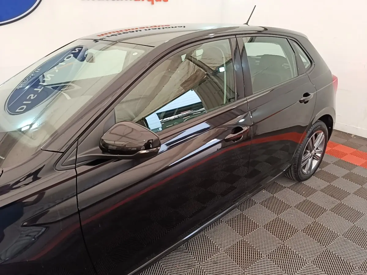 Vue latérale droite d'une Volkswagen Polo noire 2020, avec rétroviseur et poignées de porte visibles, sur sol à damiers.