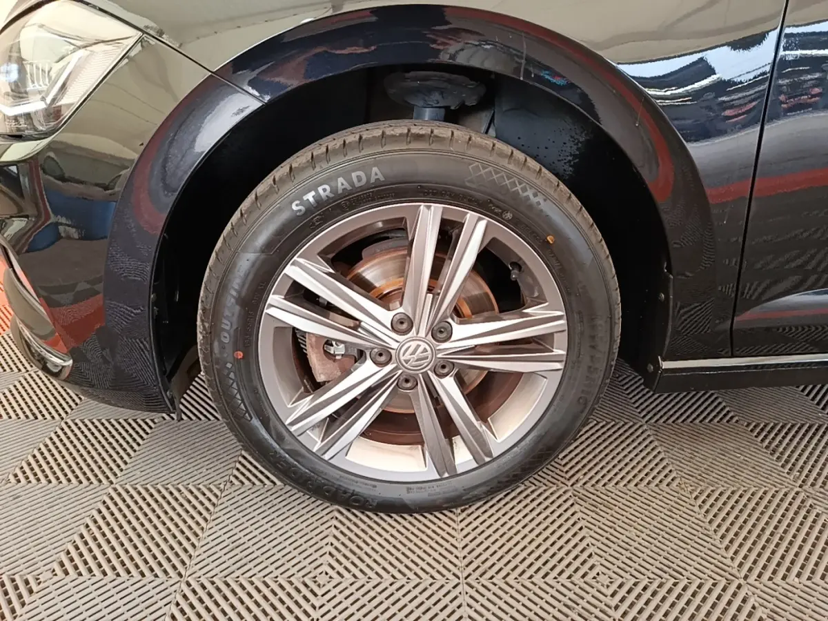 Gros plan sur la roue avant gauche noire d'une Volkswagen Polo 1.0 TSI 115 DSG7 Carat avec jante alliage argentée.
