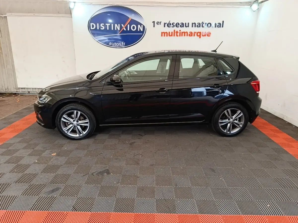 Profil côté gauche d'une Volkswagen Polo noire 2020, version Carat, sur sol damier gris et rouge en intérieur showroom.