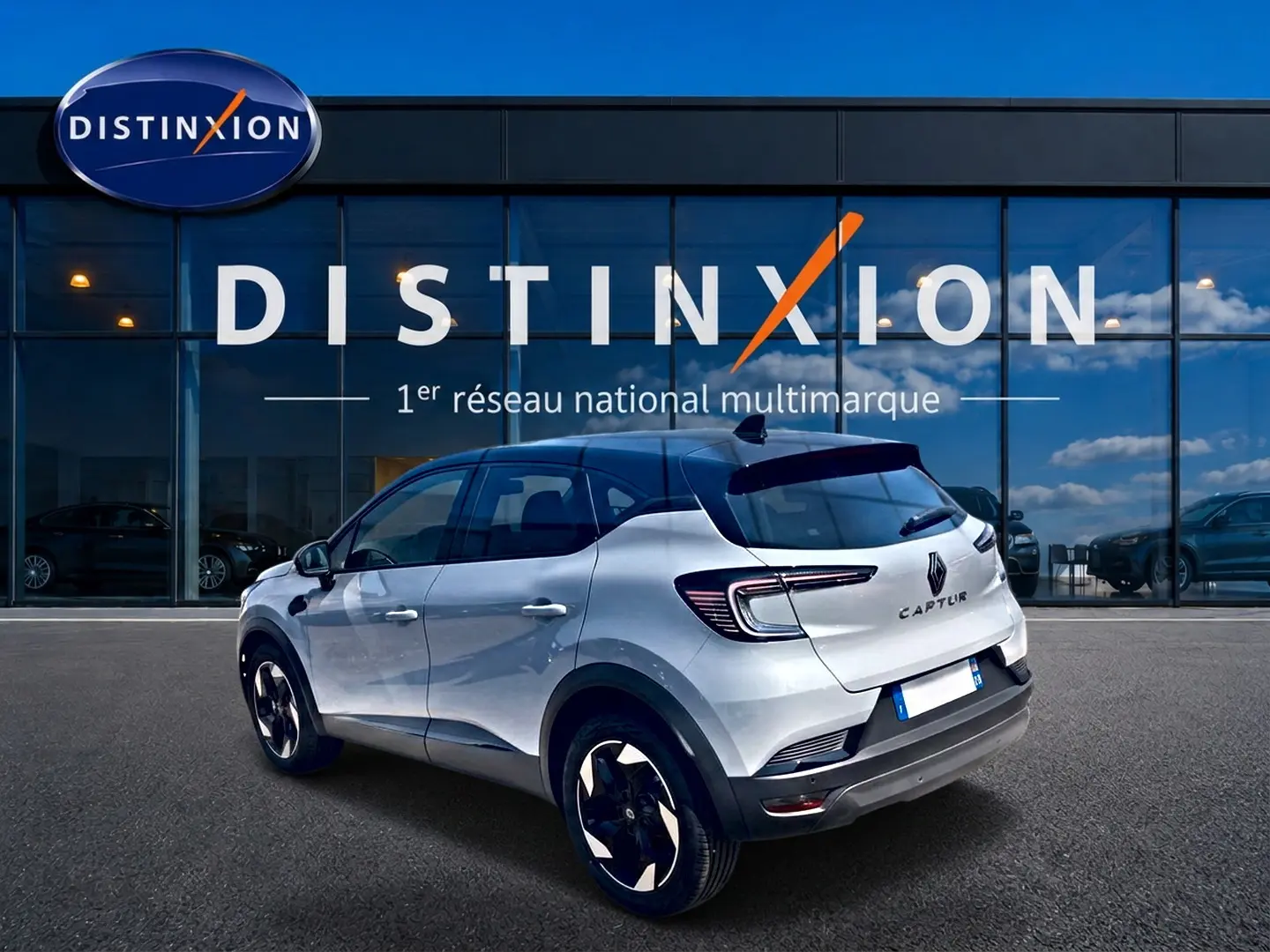 Vue 3/4 arrière droite du Renault Captur 2026 gris Rafale avec toit noir et jantes alu noires devant un showroom Distinxion.