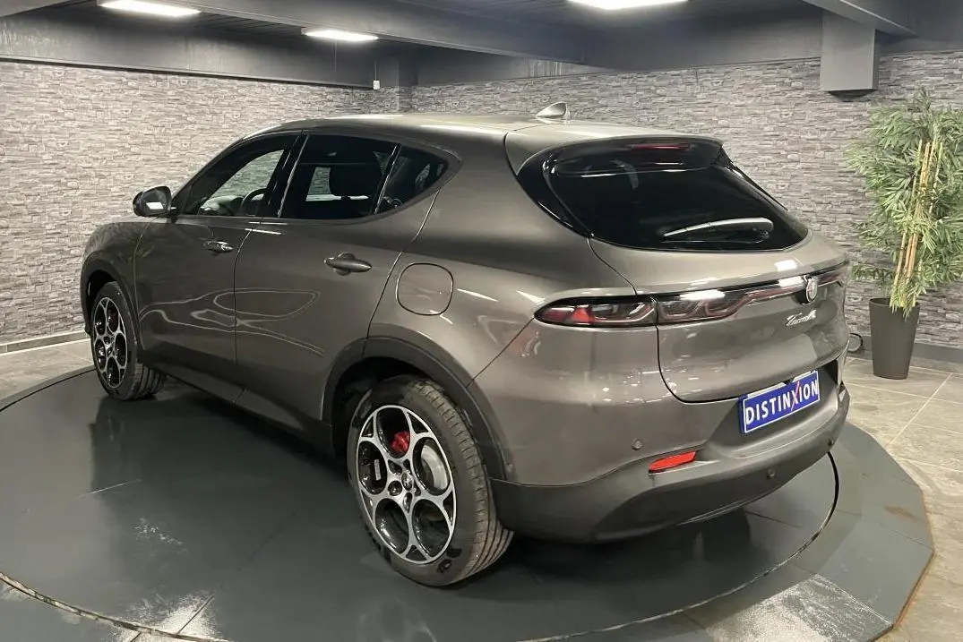Vue 3/4 arrière droite d'une Alfa Romeo Tonale gris foncé avec jantes distinctives et feux arrière LED dans un showroom.