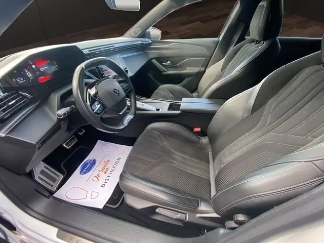 Vue intérieure côté conducteur du Peugeot 308 SW blanc nacré 2022, sièges noirs et tableau de bord moderne avec écran digital.