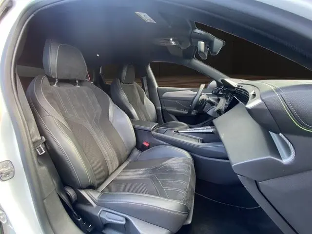 Vue intérieure côté conducteur du Peugeot 308 SW 2022, sièges en cuir noir avec surpiqûres vertes et tableau de bord moderne.