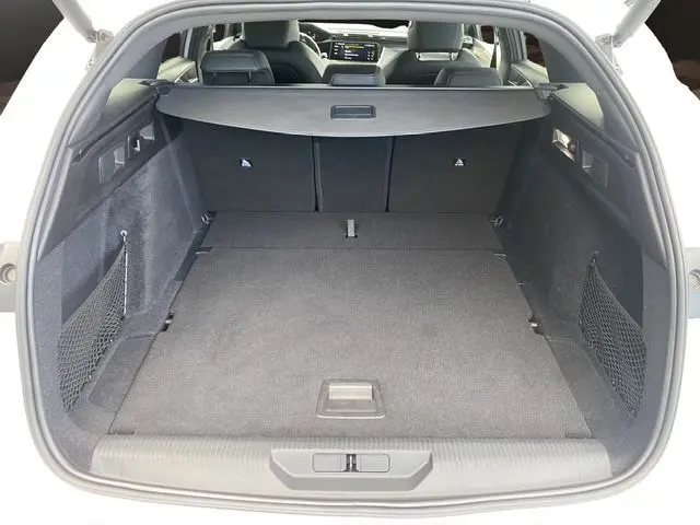 Coffre ouvert vu de l'arrière d'une Peugeot 308 SW blanc nacré, espace de chargement spacieux et tapis noir.