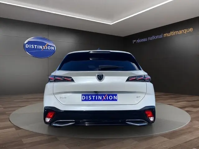 Vue arrière d'une Peugeot 308 SW blanche nacrée 2022 avec feux LED et double sortie d'échappement chromée en showroom.