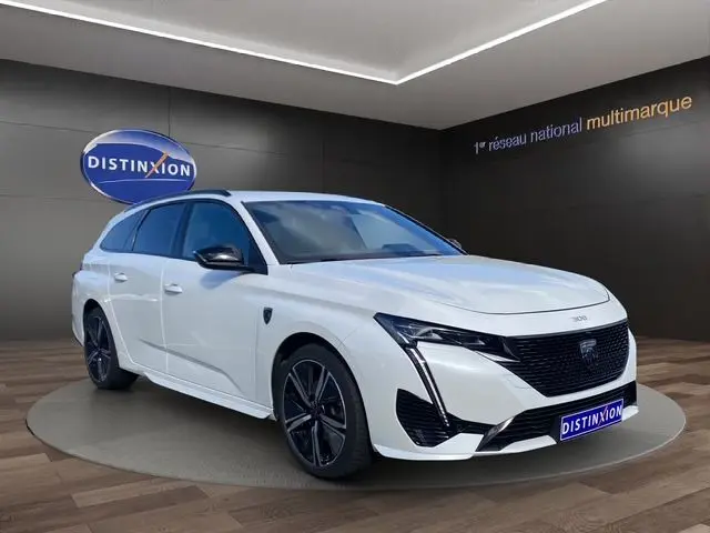 Peugeot 308 SW blanc nacré vue 3/4 avant droit, avec calandre noire et jantes alliage foncé en showroom.