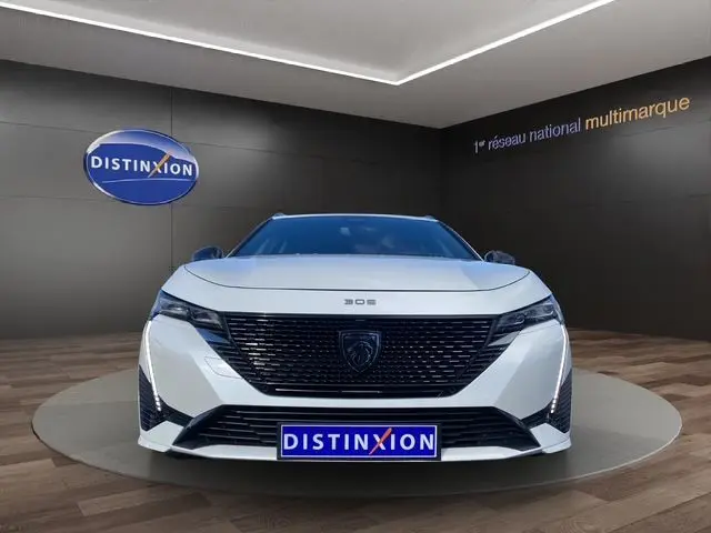Vue frontale d'une Peugeot 308 SW blanc nacré avec calandre noire et éclairage LED, en showroom Distinxion.