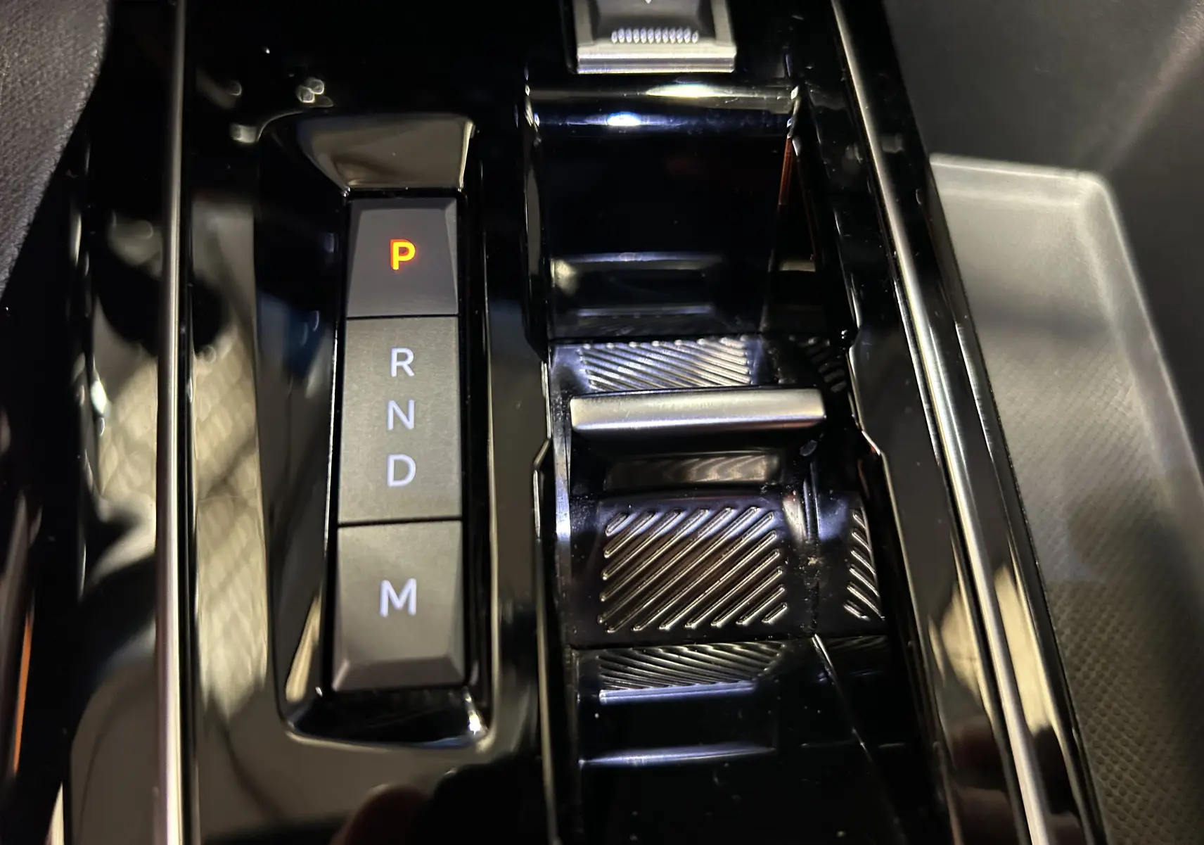 Gros plan sur la console centrale noire brillante du Peugeot 3008 Hybrid avec levier de vitesses automatique et indicateur P allumé.