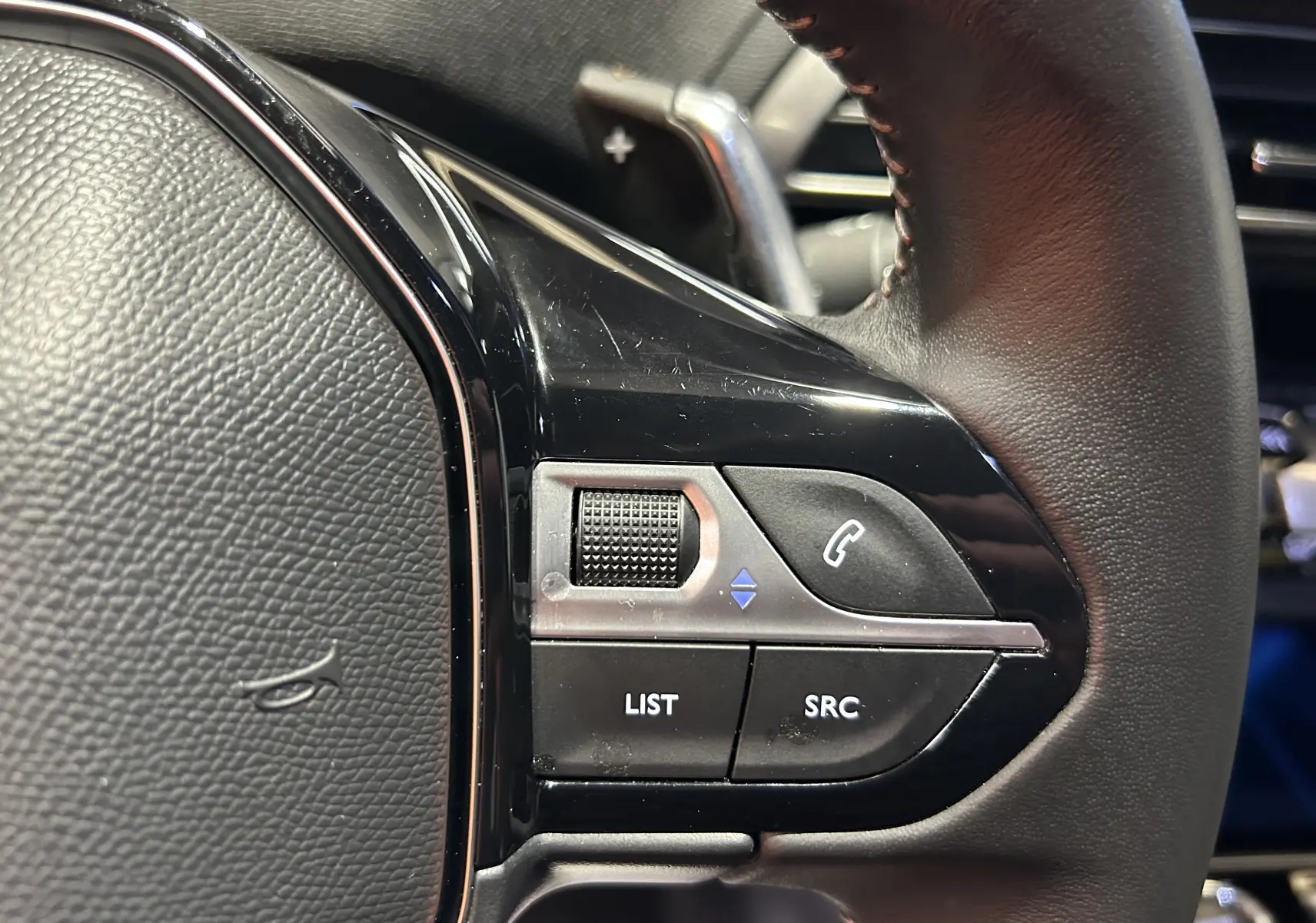 Détail du volant cuir du Peugeot 3008 Hybrid 2024 montrant les commandes audio et téléphone côté gauche.