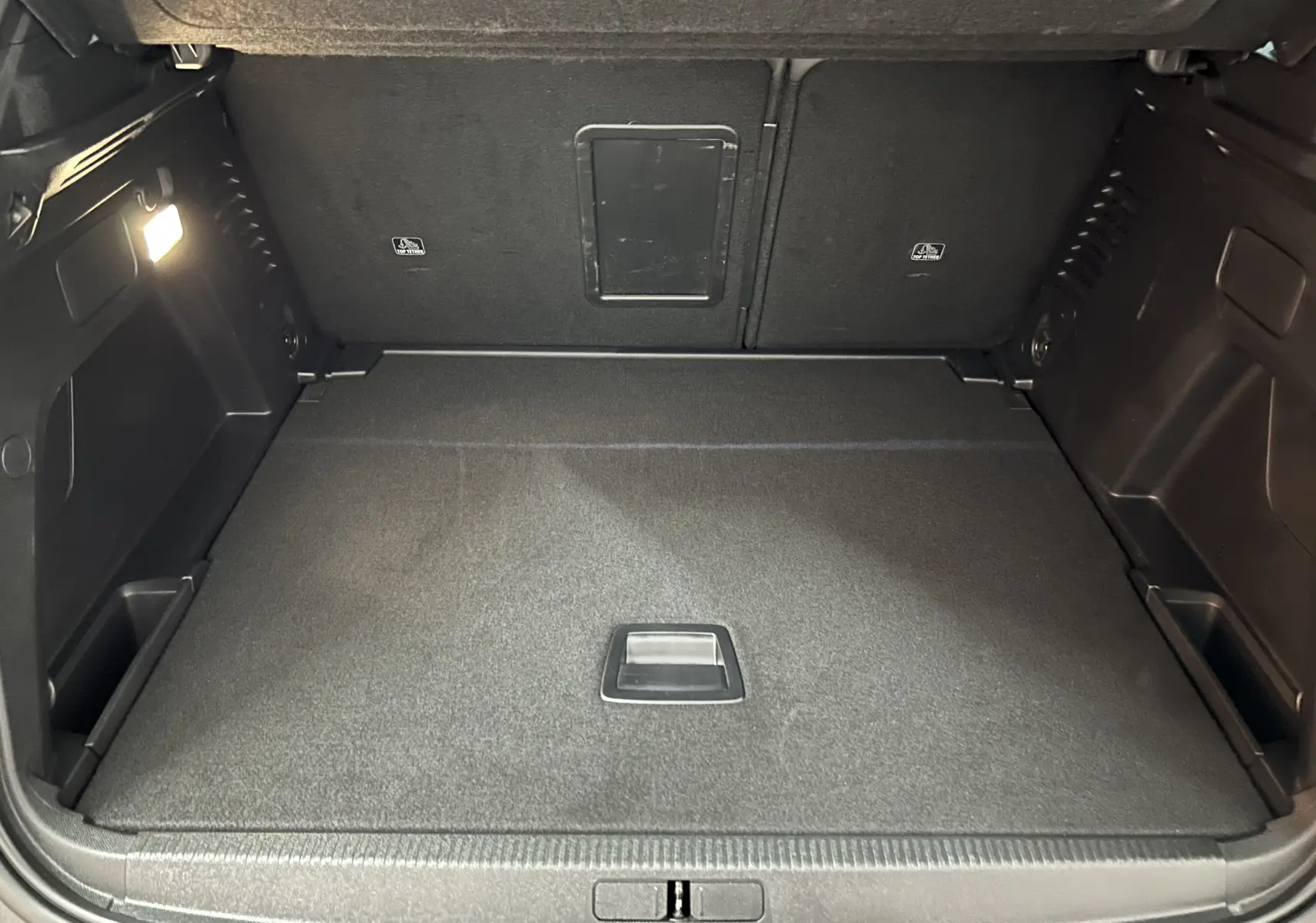 Coffre ouvert en vue arrière d’un Peugeot 3008 Hybrid gris, montrant un espace de chargement propre et éclairé.