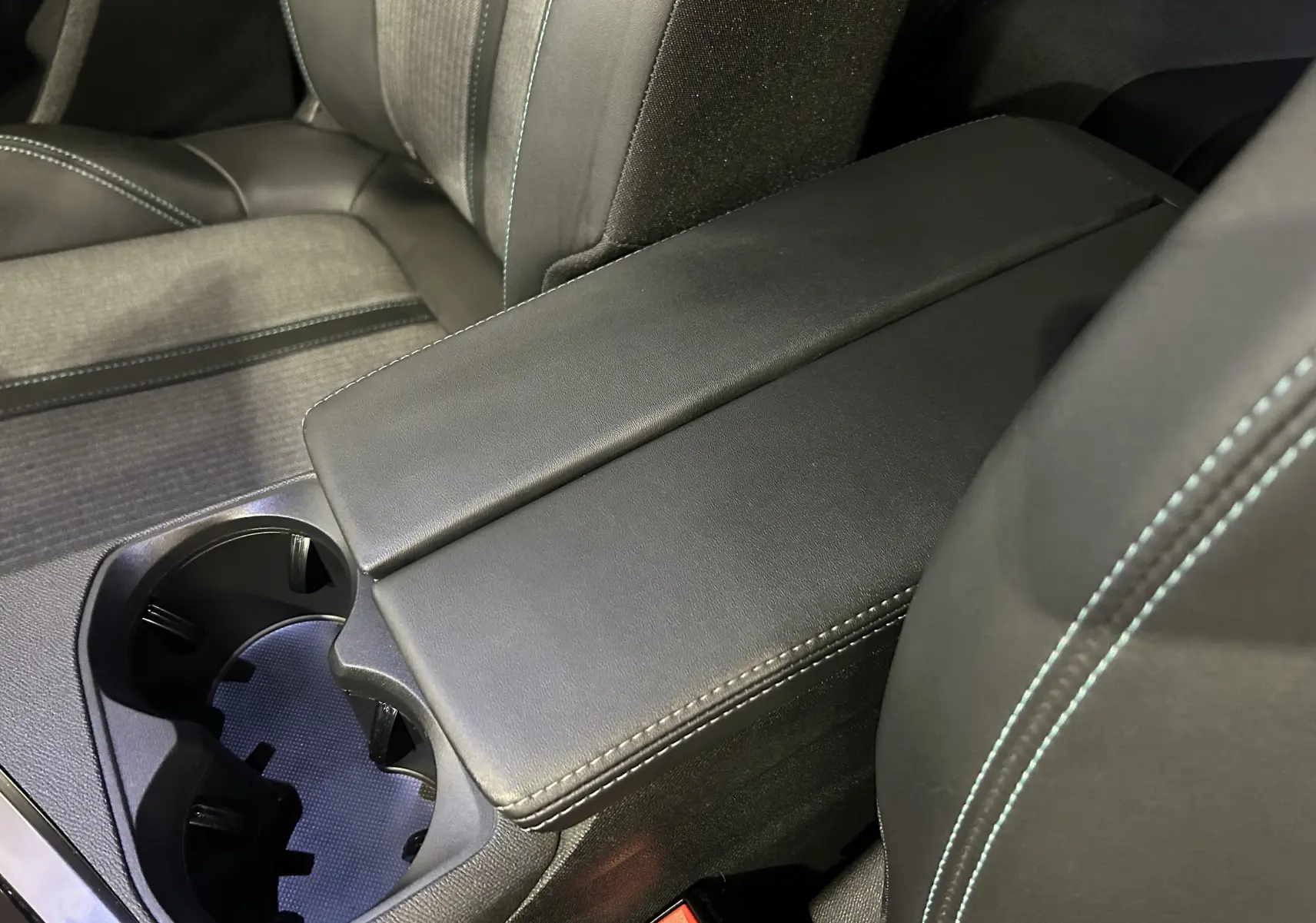 Détail de l’accoudoir central noir avec surpiqûres bleues et porte-gobelets du Peugeot 3008 Hybrid 2024.