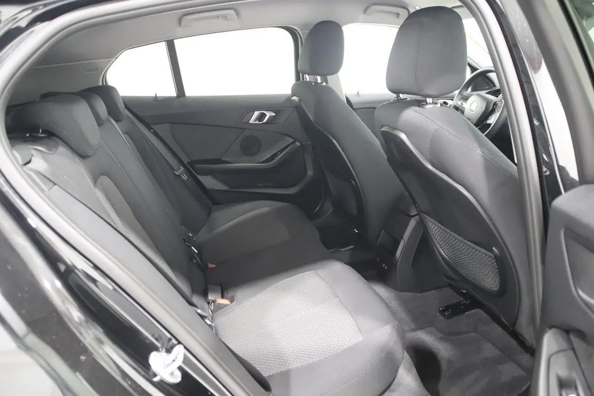 Vue intérieure côté gauche des sièges arrière noirs en tissu d'une BMW Série 1 116d 2023 avec porte ouverte.