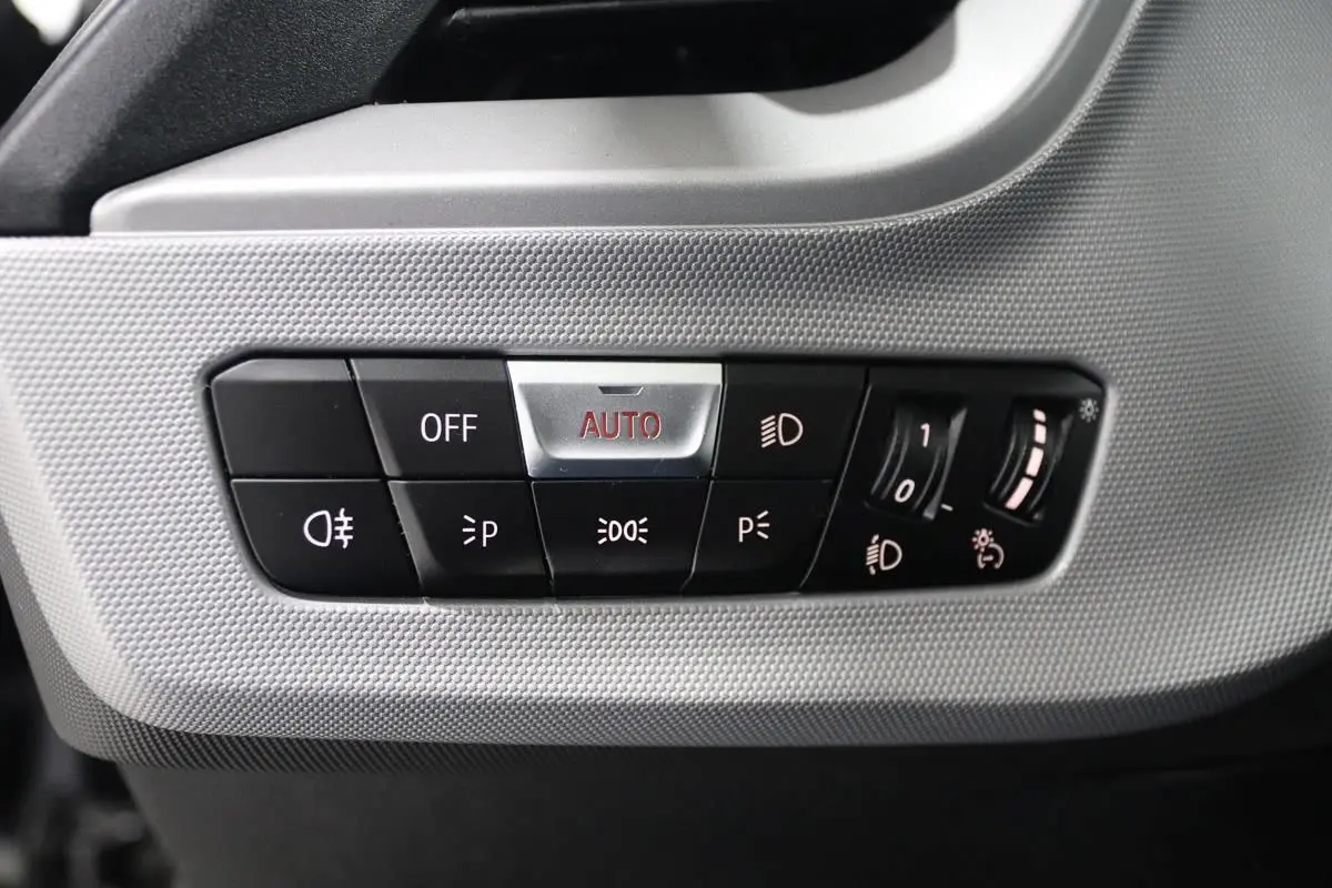 Gros plan sur les commandes d’éclairage à gauche du tableau de bord de la BMW Série 1 116d noire de 2023.