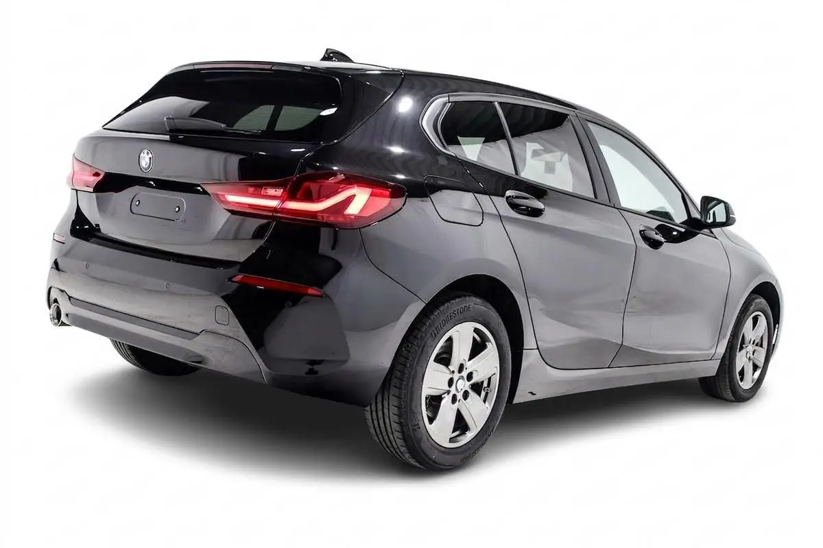 BMW Série 1 116d noire vue en 3/4 arrière droit, avec feux arrière allumés et jantes alliage cinq branches.