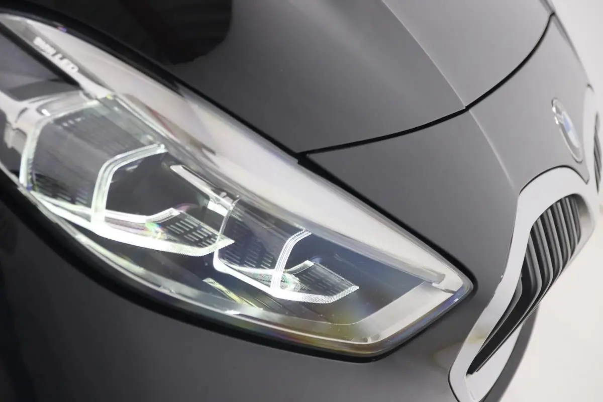 Gros plan sur le phare avant gauche d’une BMW Série 1 noire 2023, mettant en valeur la calandre et les lignes du capot.