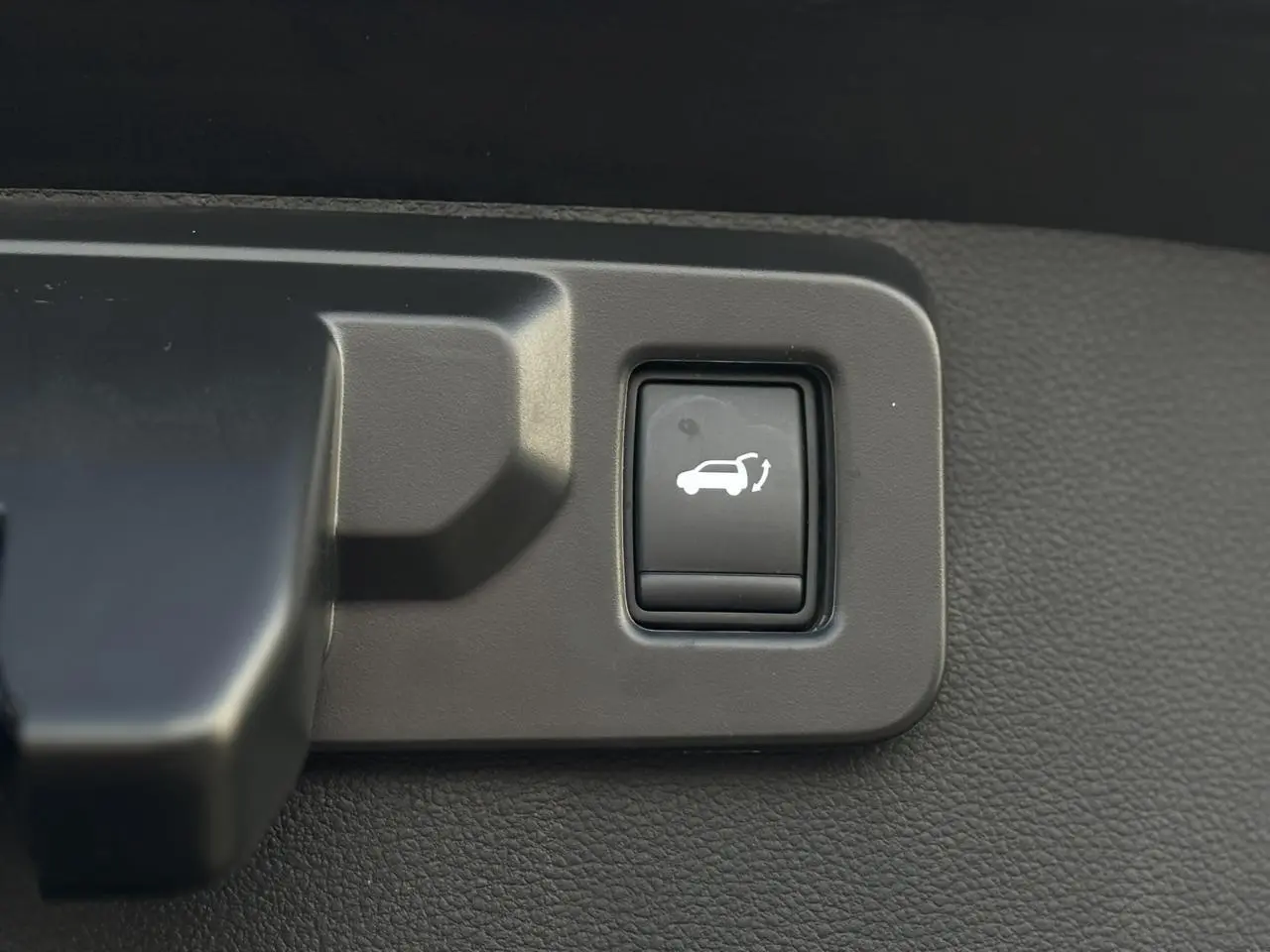 Bouton d'ouverture du hayon mains libres sur tableau de bord intérieur du Renault Symbioz noir étoilé.