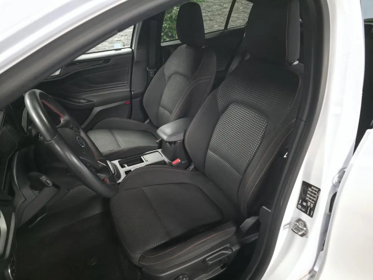 Vue intérieure côté conducteur de la Ford Focus blanche 2024, sièges tissu ST-Line noirs avec surpiqûres rouges.