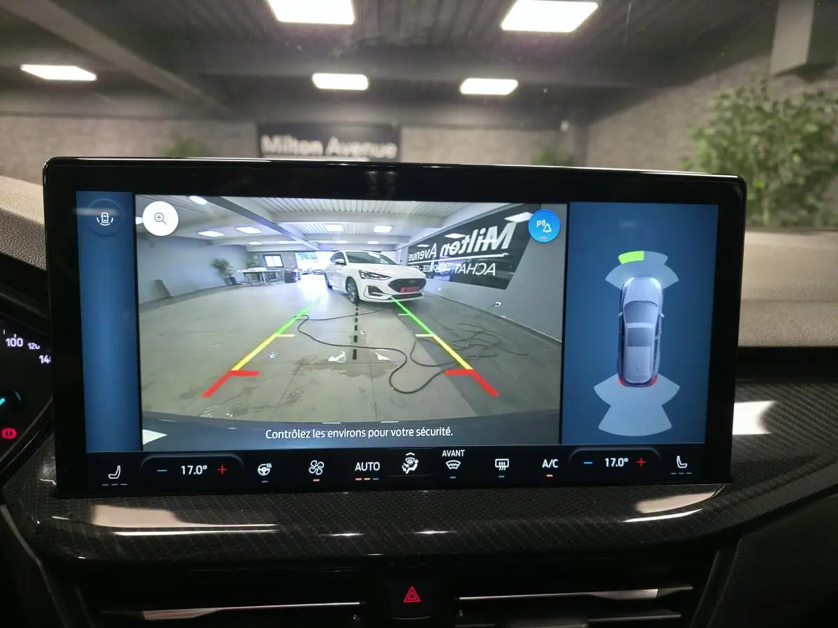 Écran multimédia montrant la caméra de recul avec vue 3/4 avant d'une Ford Focus blanche en intérieur.