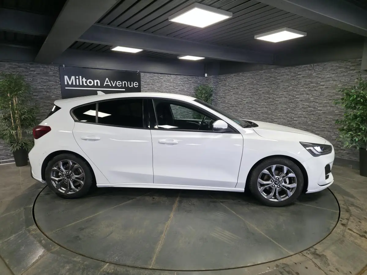 Ford Focus blanche 2024 vue de profil côté gauche, jantes alliage 17 pouces et vitres surteintées.