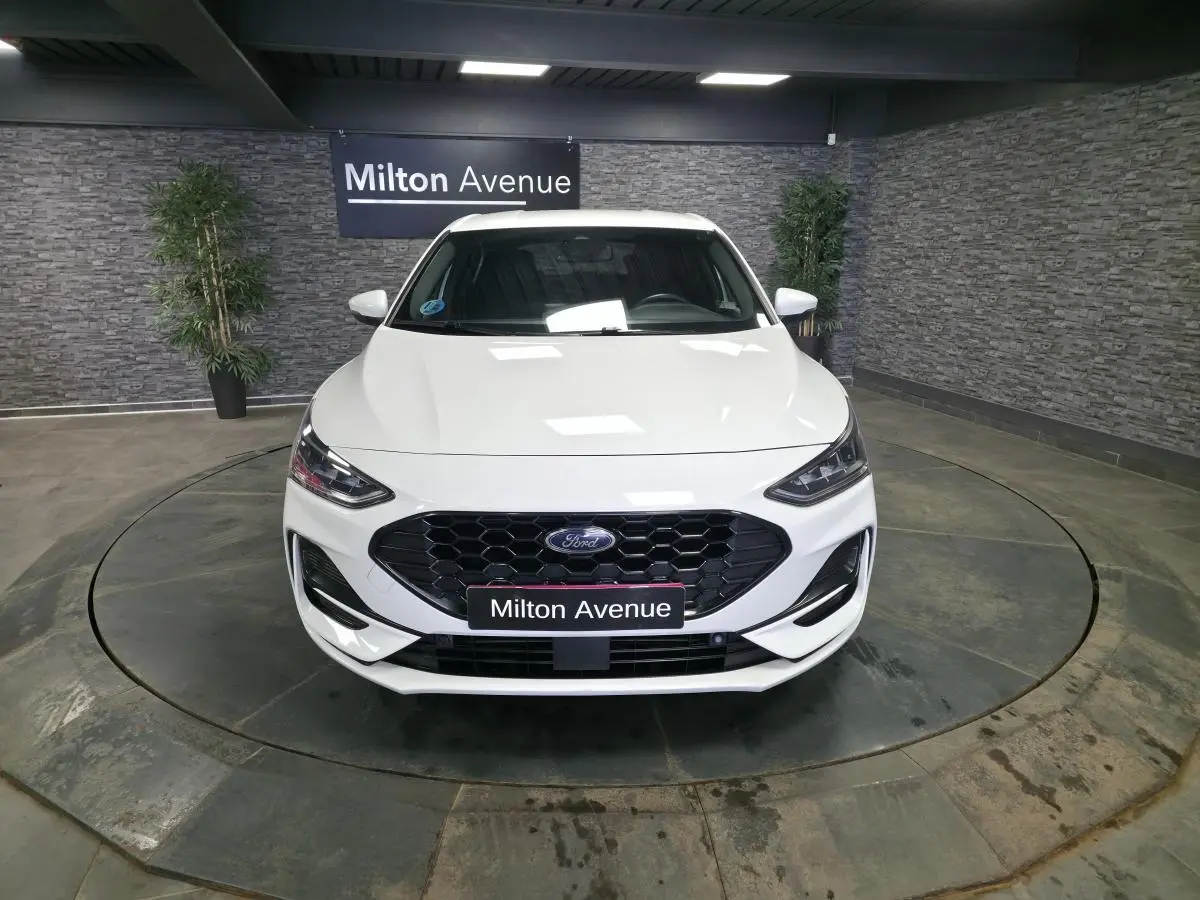 Vue avant d'une Ford Focus blanche 2024 avec calandre noire hexagonale et phares LED dans un showroom.