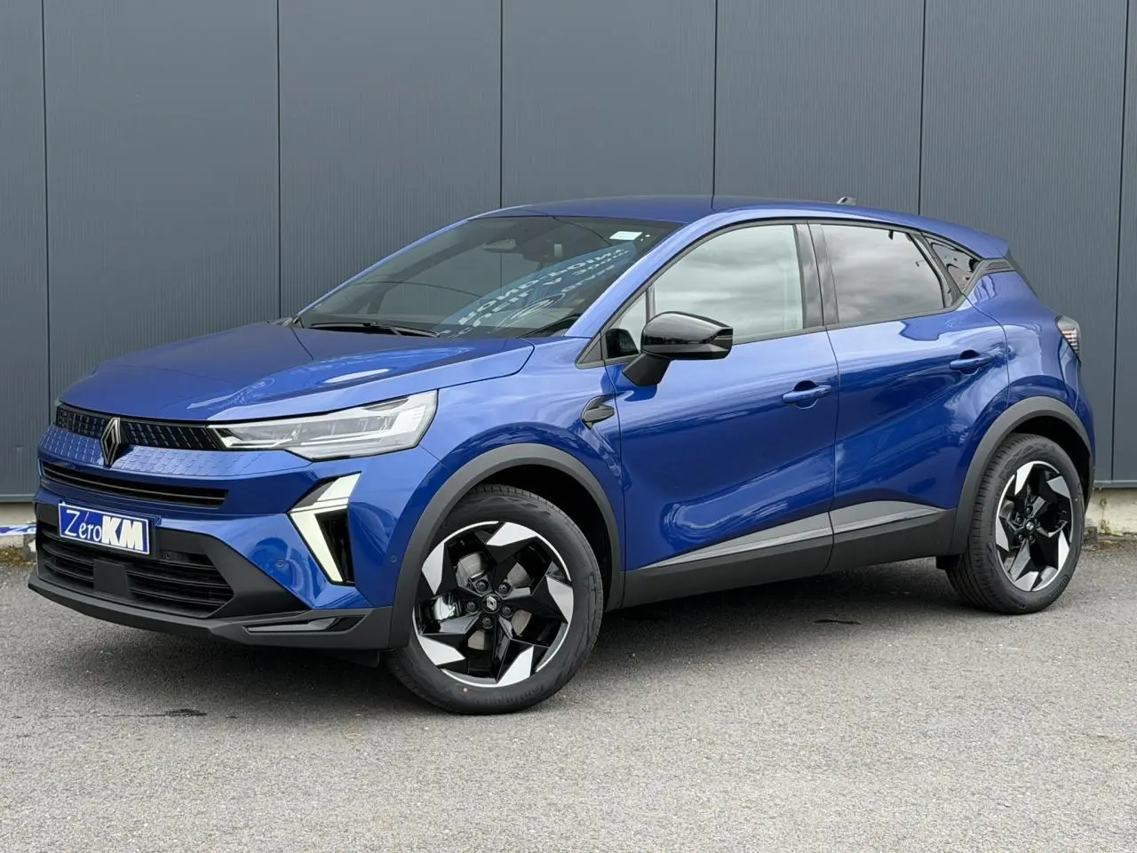 Renault Captur 2026 bleu Iron en 3/4 avant droit, avec jantes aluminium noires et rétroviseurs noirs brillants.