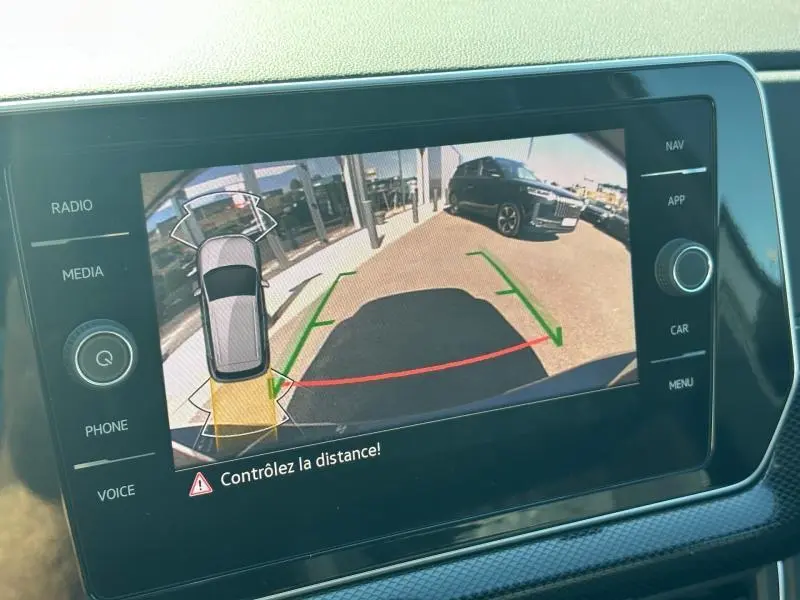 Vue écran caméra de recul du Volkswagen T-Cross gris cendré, montrant l’arrière avec guidage de trajectoire et véhicule noir en arrière-plan.