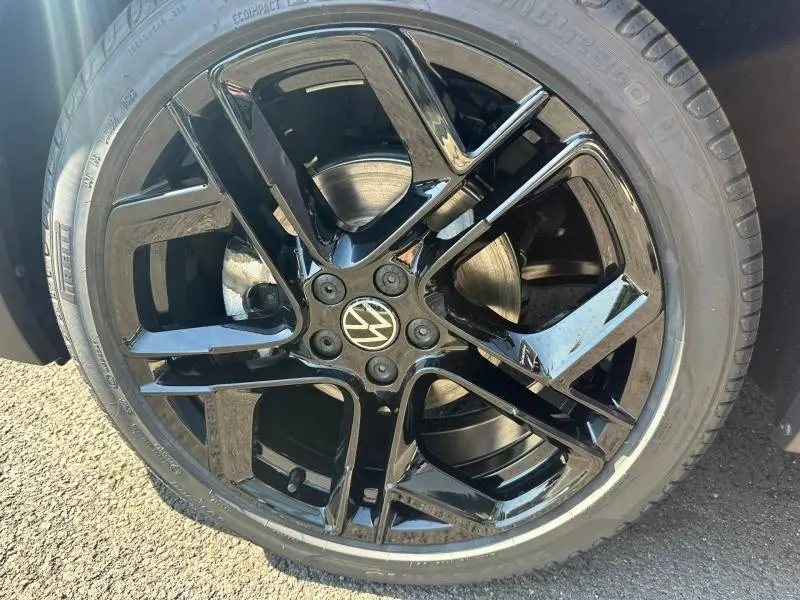 Gros plan sur la jante noire brillante à cinq branches du Volkswagen T-Cross gris cendré, avec logo VW au centre.