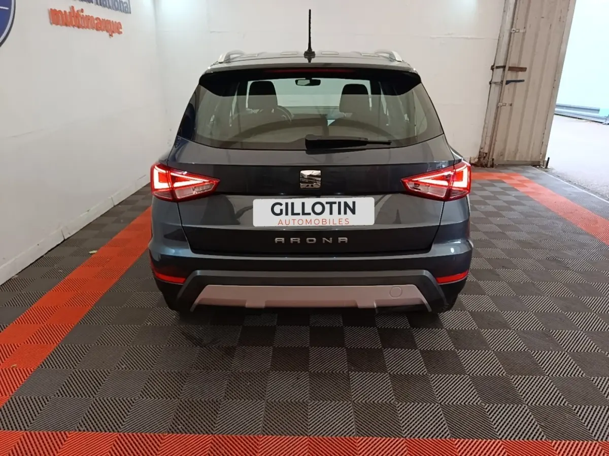 Vue arrière d'un SEAT Arona gris clair avec feux arrière allumés dans un garage au sol damier noir et rouge.