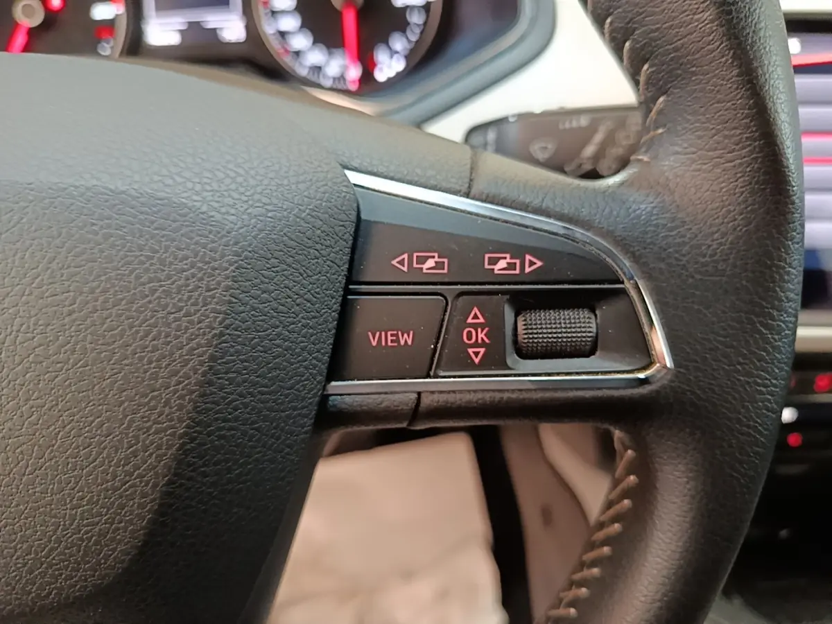 Gros plan sur les commandes à droite du volant cuir du SEAT Arona gris clair, avec tableau de bord numérique en arrière-plan.