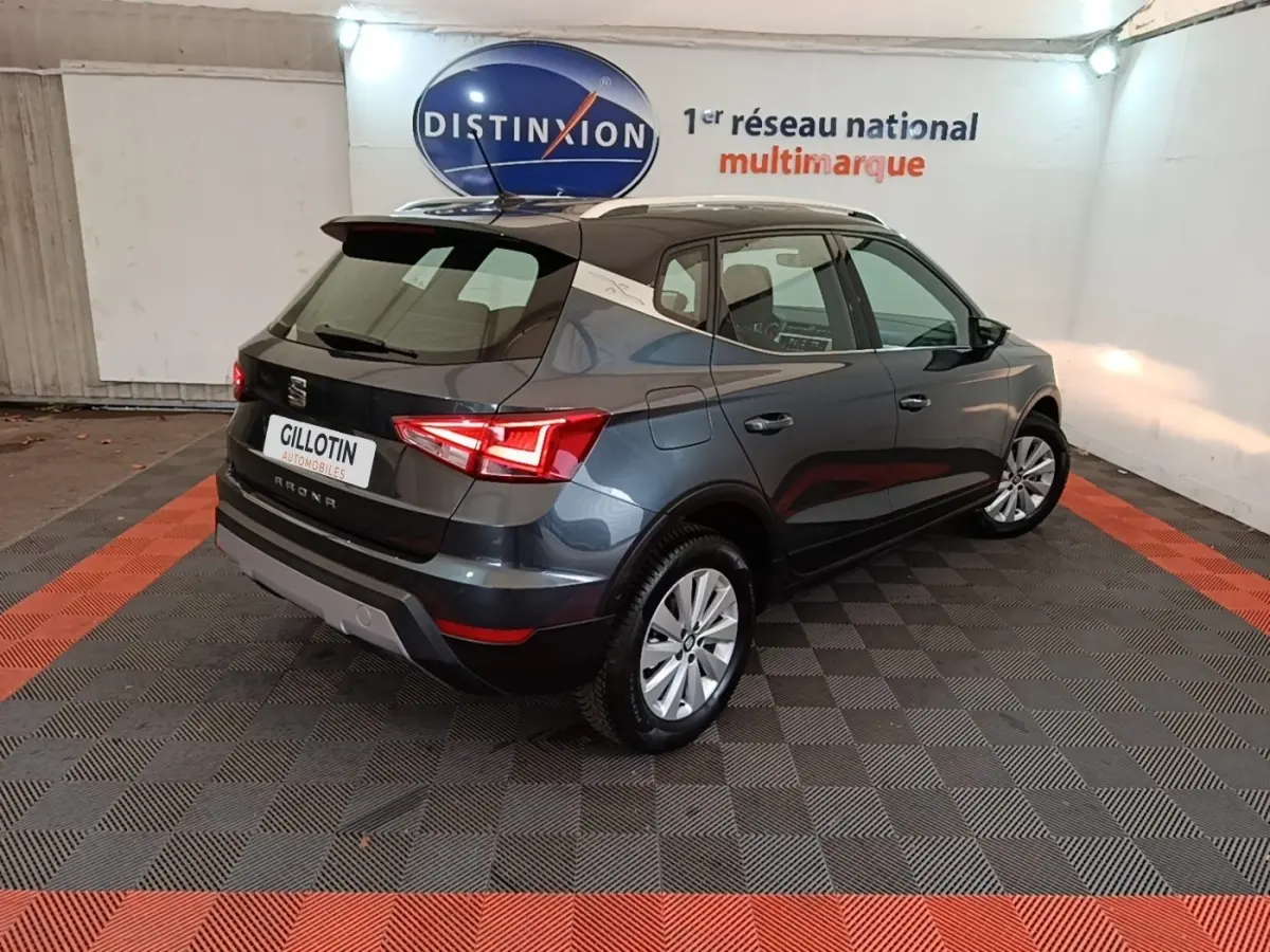 Vue 3/4 arrière droite d'un SEAT Arona gris clair 2019 dans un showroom avec éclairage intérieur.