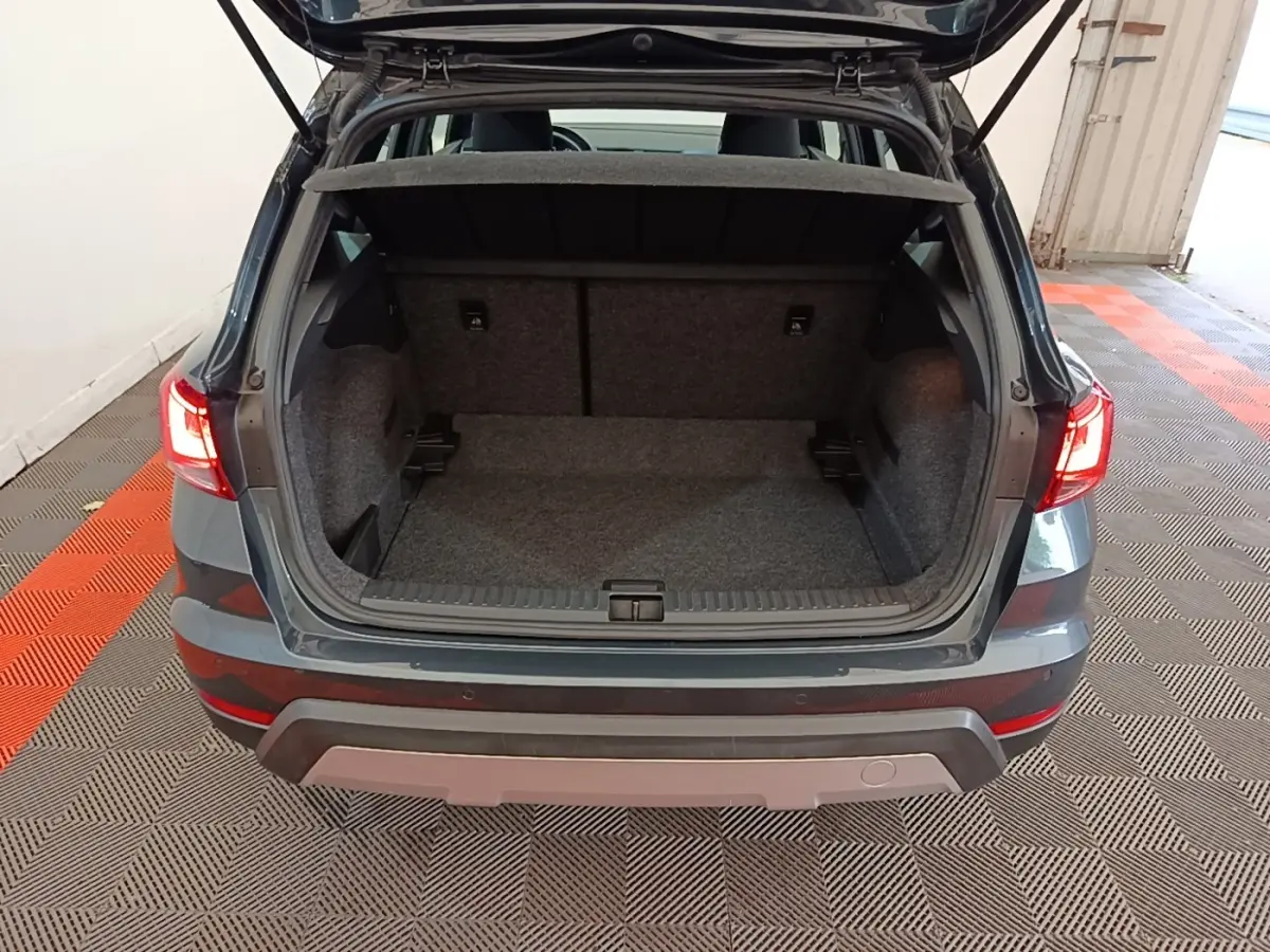 Vue arrière du coffre ouvert d'un SEAT Arona gris clair, intérieur spacieux et tapis gris visible.