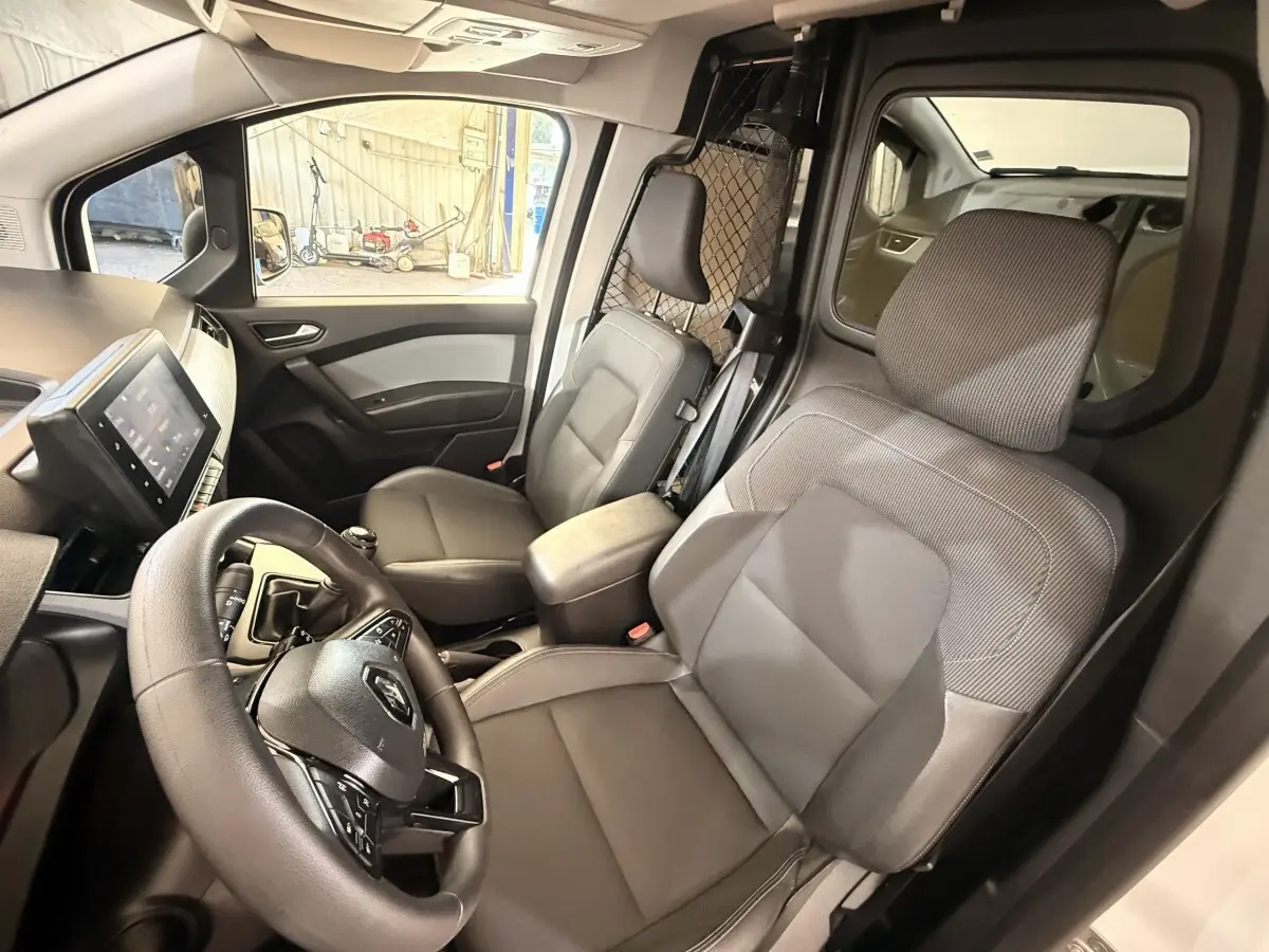 Vue intérieure côté conducteur du Renault Kangoo blanc 2022, avec volant, sièges gris et cloison métallique de séparation.