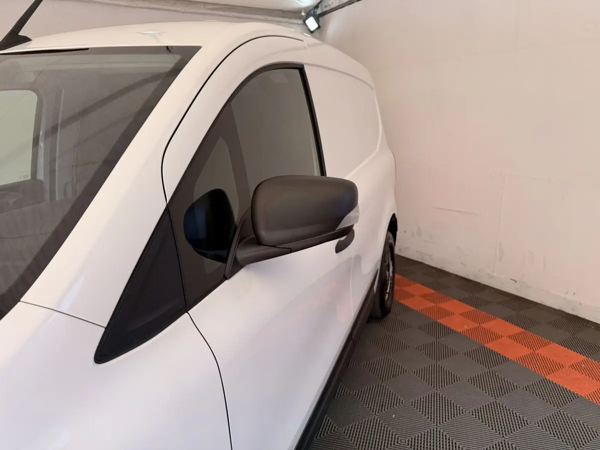 Vue de côté droit d’un Renault Kangoo blanc 2022, avec rétroviseur noir, stationné sur un sol à damiers gris et orange.