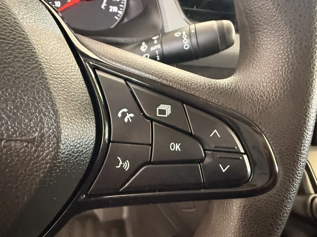 Gros plan sur les commandes multifonctions noires du volant du Renault Kangoo blanc de 2022, avec boutons de téléphone et navigation.