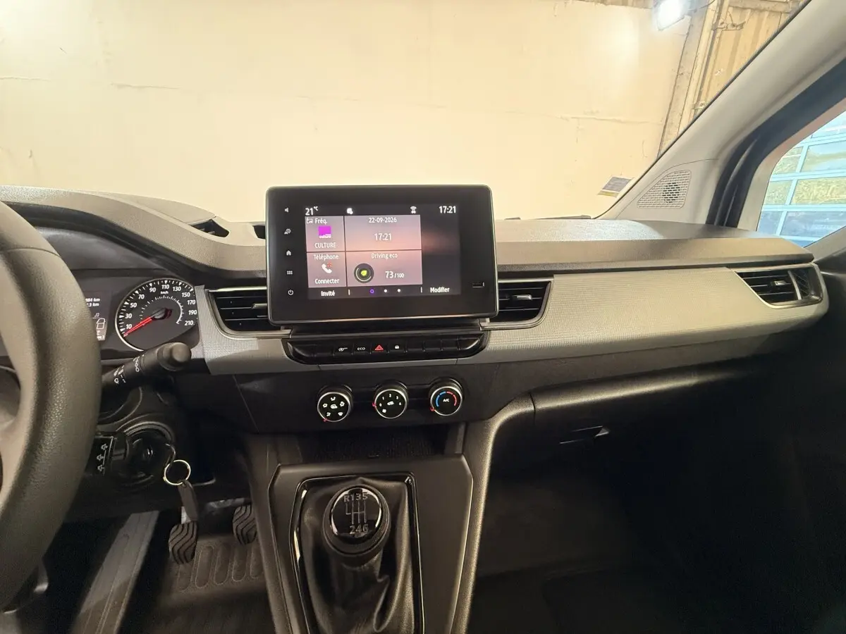 Vue intérieure du tableau de bord du Renault Kangoo blanc 2022, avec écran tactile central et levier de vitesse manuel visible.