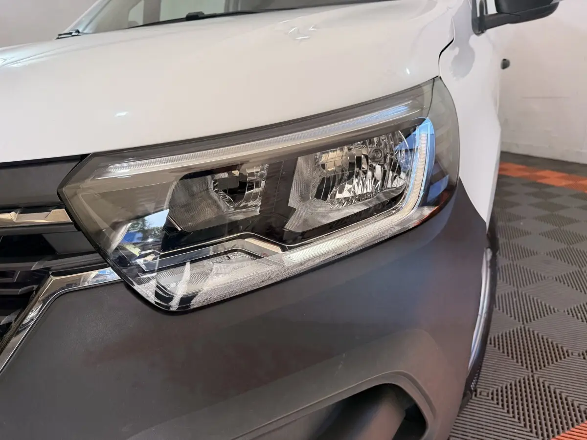 Gros plan sur le phare avant droit du Renault Kangoo blanc 2022 avec calandre noire et pare-chocs gris.