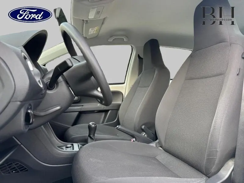 Intérieur avant de la Volkswagen Up blanche, vue côté conducteur montrant sièges en tissu noir et volant réglable.