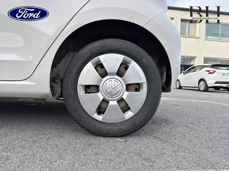 Gros plan sur la roue arrière droite d'une Volkswagen Up blanche Candy avec enjoliveur VW visible sur parking.