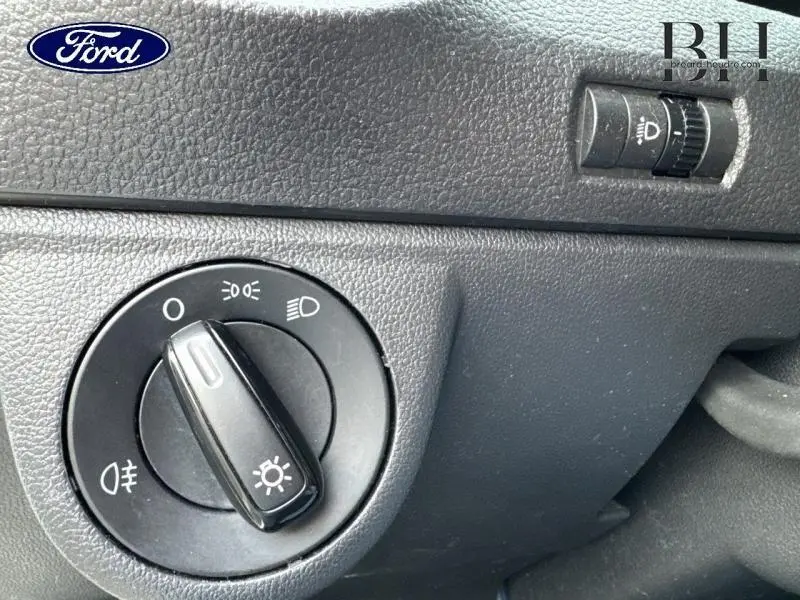 Gros plan sur le bouton de commande des phares noirs dans l'habitacle d'une Volkswagen Up blanche vue côté conducteur.