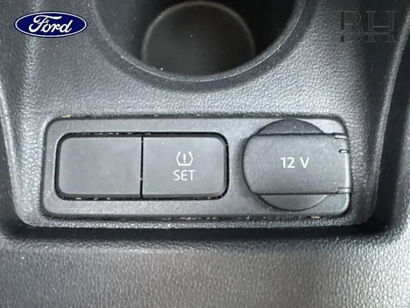 Gros plan sur la console centrale d'une Volkswagen Up blanche montrant la prise 12V et le bouton de réglage de la pression des pneus.