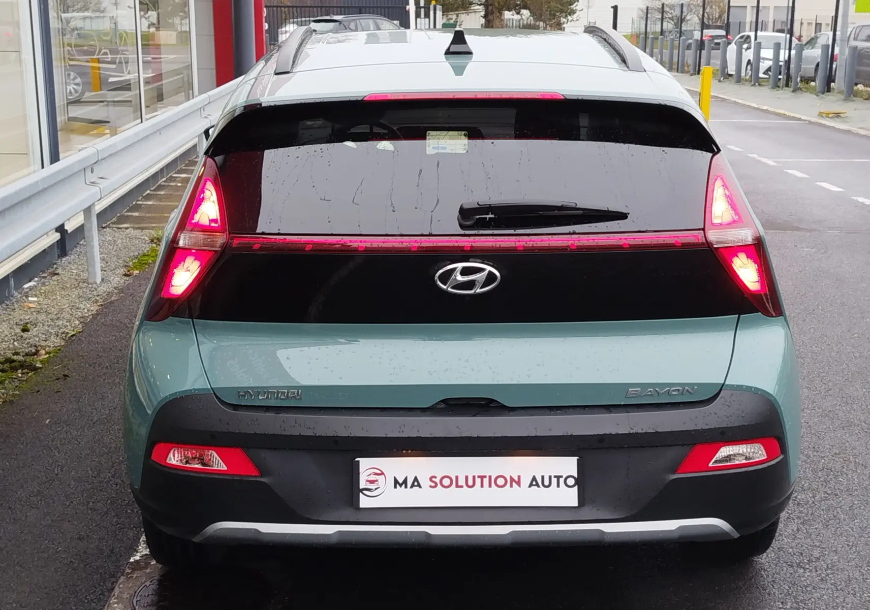 Vue arrière d'une Hyundai Bayon 2022 couleur Elemental Brass Metal avec feux allumés et hayon noir brillant.