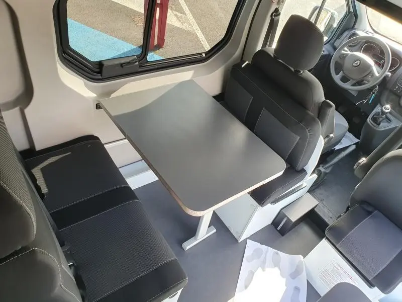 Vue intérieure du Renault Trafic Fourgon L2H1 2022, montrant la banquette noire et la table centrale grise près de la fenêtre.